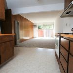 Viking Apartments kitchen with dark wooden cabinets, orange counters and light tile floors looking through to living room